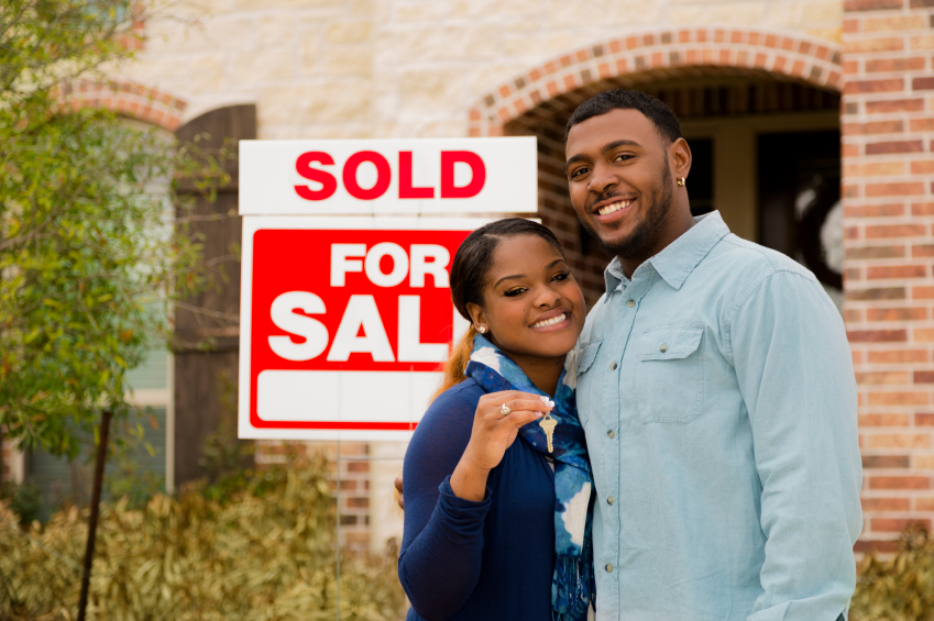 Young couple with house keys in front of Sold sign