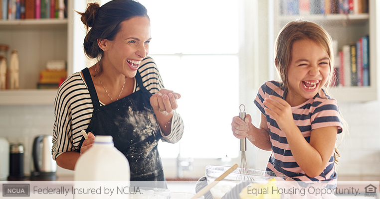 woman with flour on her apron laughing while baking with daughter